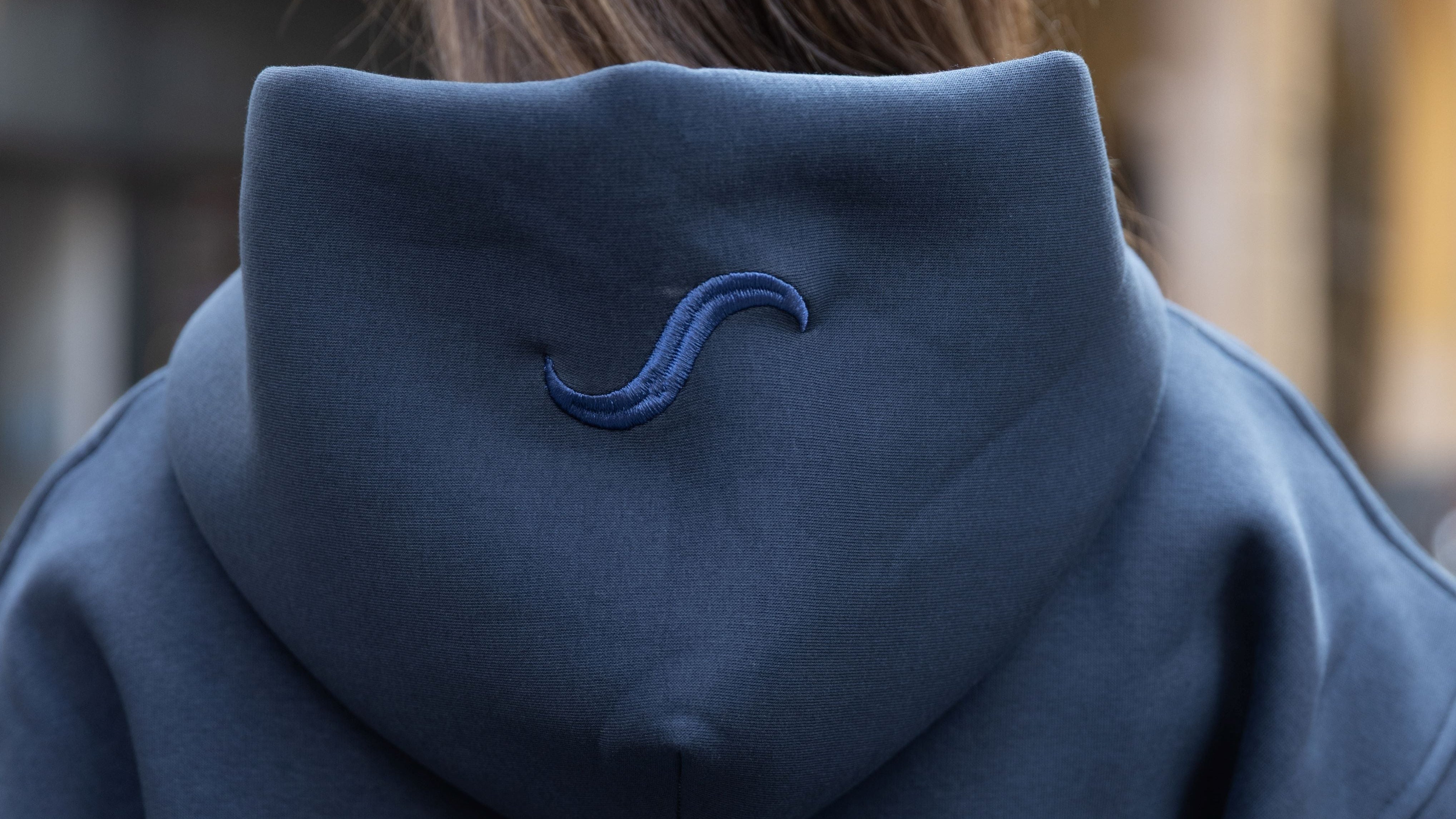 Person wearing a dark blue hoodie with a logo on the back, standing outdoors.