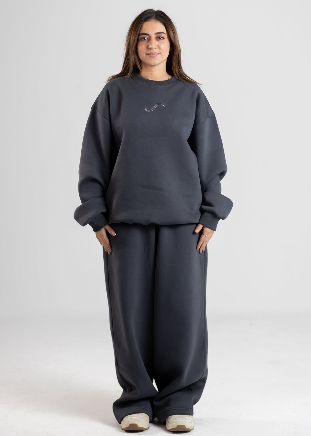 Person wearing a dark gray sweatshirt and pants on a white background